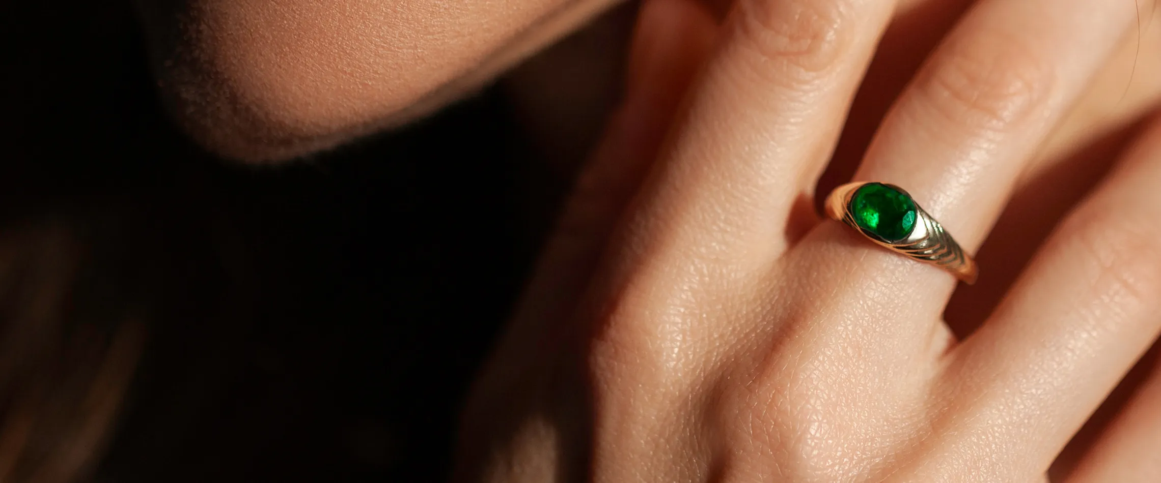 Close-up of a hand wearing a gold ring with a green gemstone. Click to shop now at Synder Jewelers in Longmont.