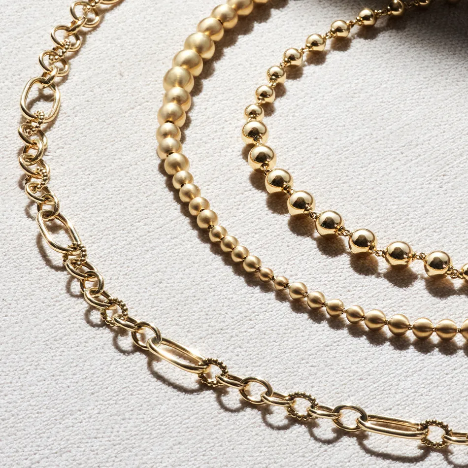 Three elegant gold necklaces of varying styles and sizes displayed on a textured background.