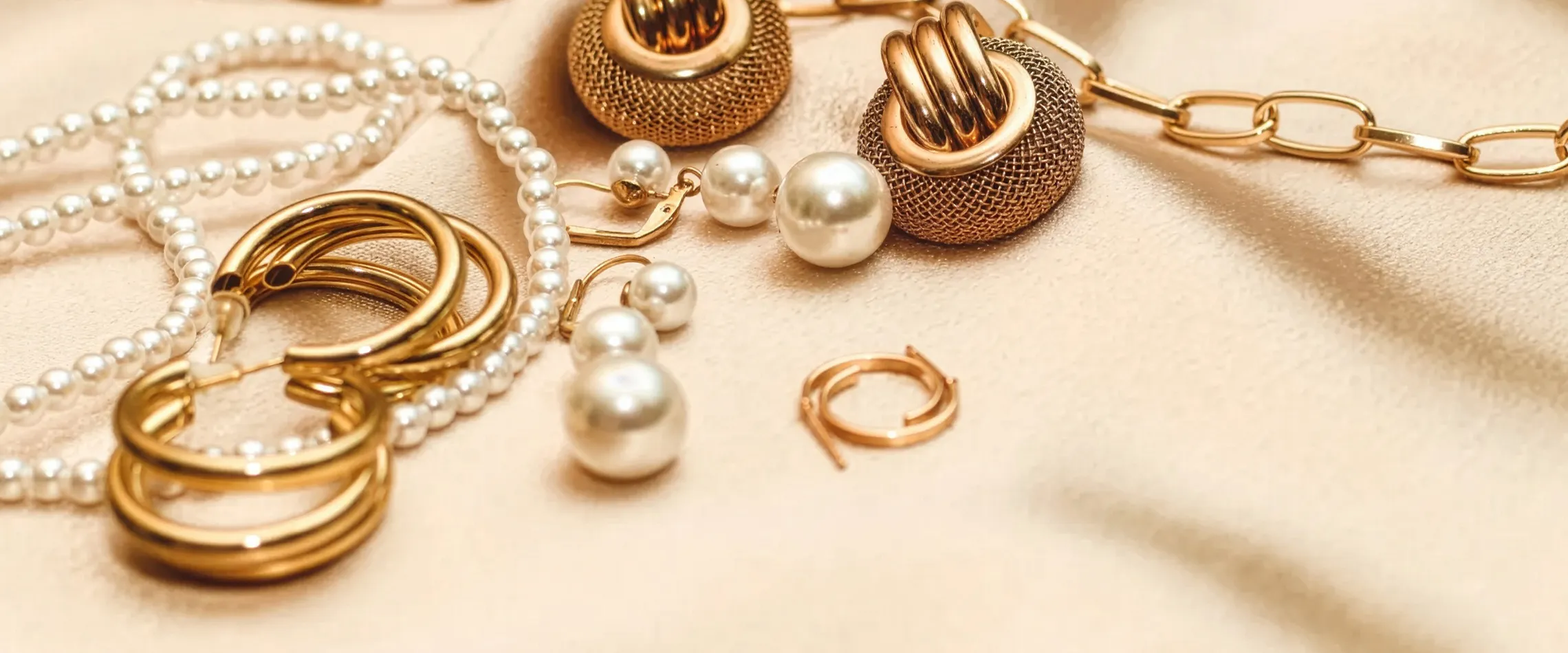 Elegant assortment of gold and pearl jewelry pieces on a soft fabric background.