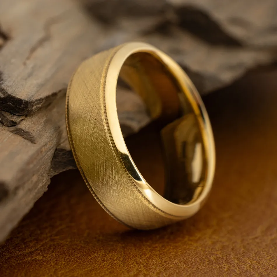 Gold wedding band with a brushed finish, displayed on a textured surface. Visit Synder Jewelers for more wedding bands.