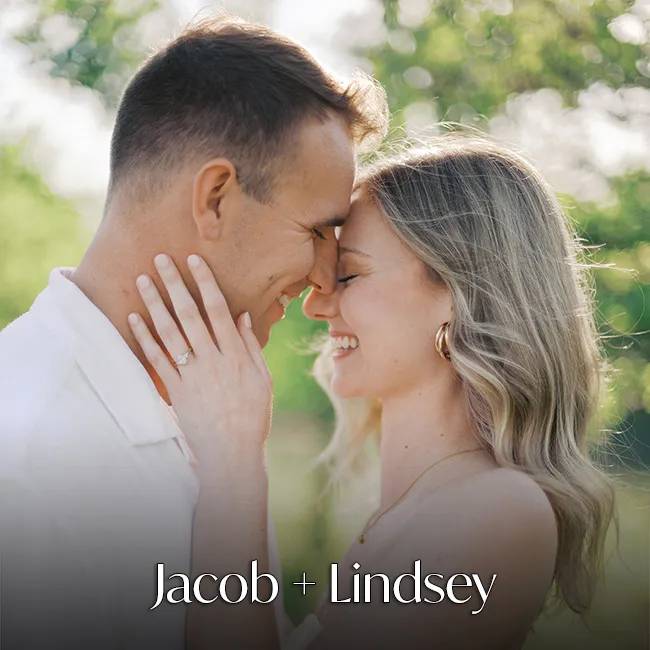 A smiling couple with an engagement ring, outside at night.
