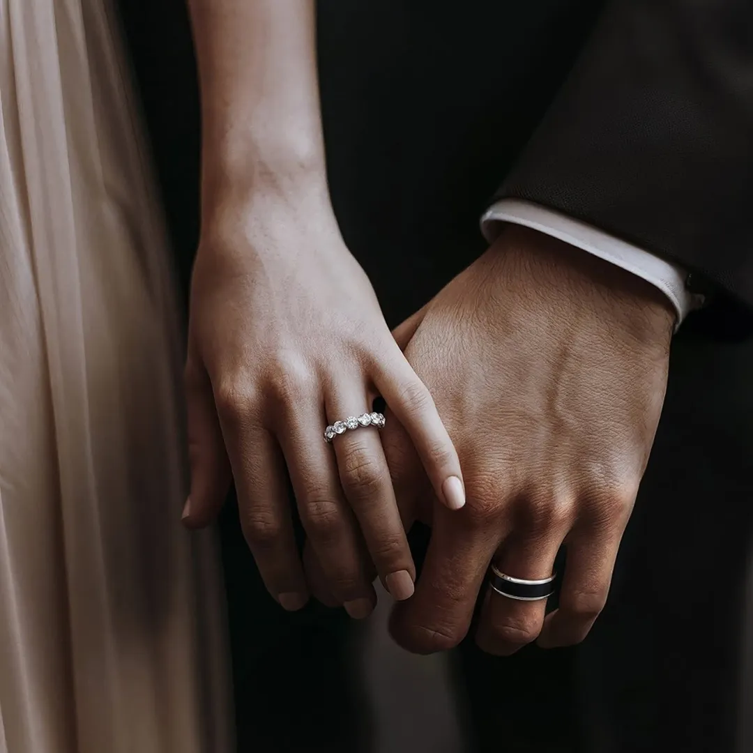 Couple holding hands wearing their wedding bands, with an engagement ring sitting alongside the band