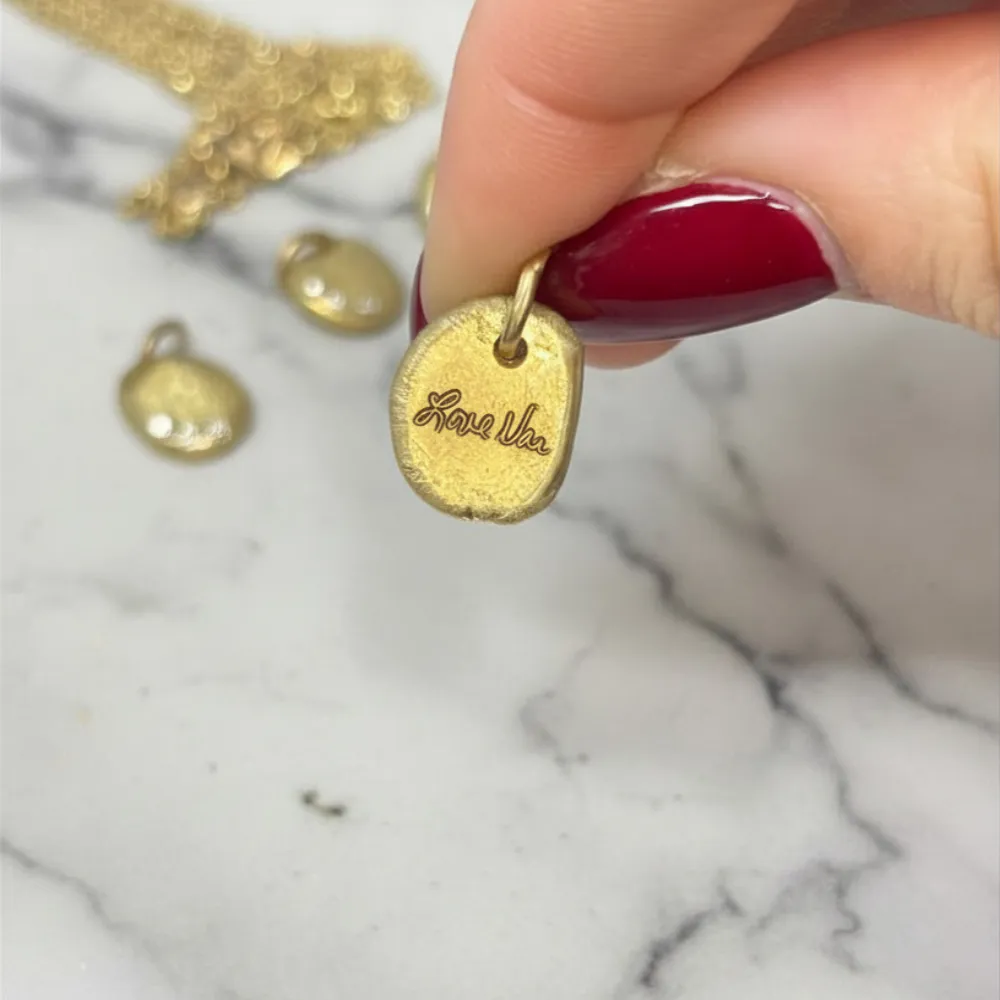 Close-up of a small gold pendant engraved with a handwritten signature reproduction