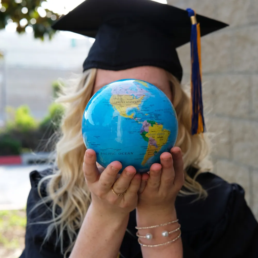 College graduate in cap and gown holding a Mova kinetic globe — Mova graduation gifts at SVS Fine Jewelry Long Island