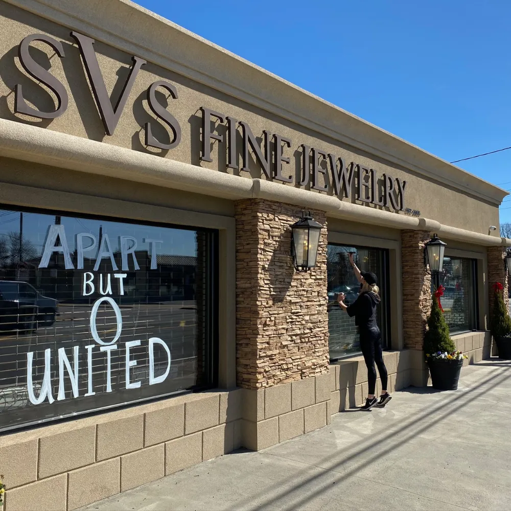 Morgan Nicki Saatchi painting 'Apart but United' on the SVS Fine Jewelry storefront windows during the COVID-19 closure in March 2020