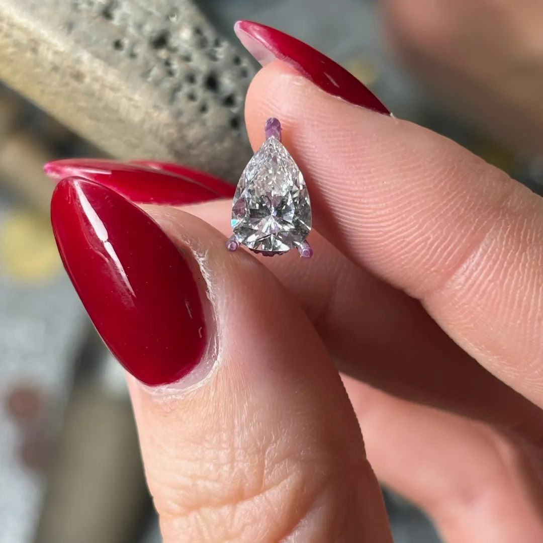 A client's loose pear shaped diamond held between the fingertips at the SVS Fine Jewelry bench in Oceanside, NY