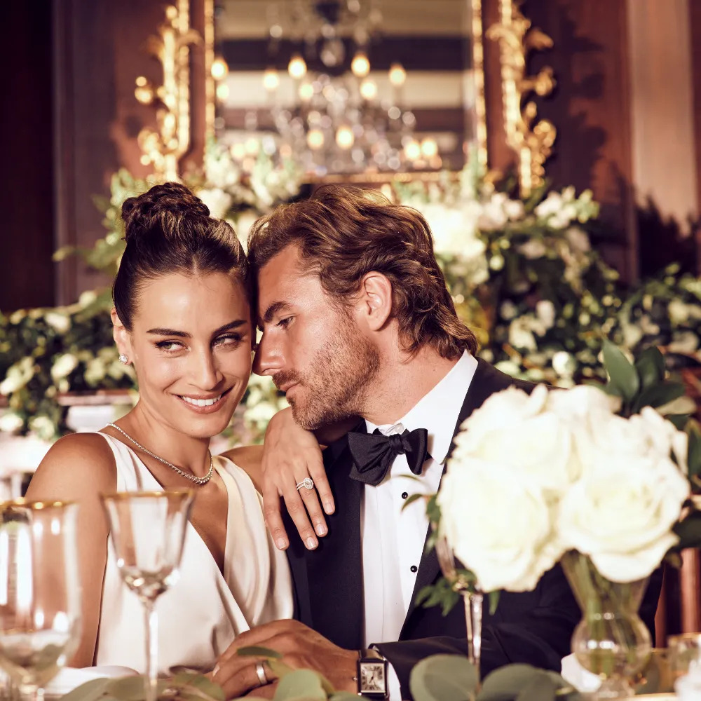 Husband and wife at a candle-lit wedding table, groom wearing a luxury wristwatch and band from SVS Fine Jewelry Oceanside Long Island