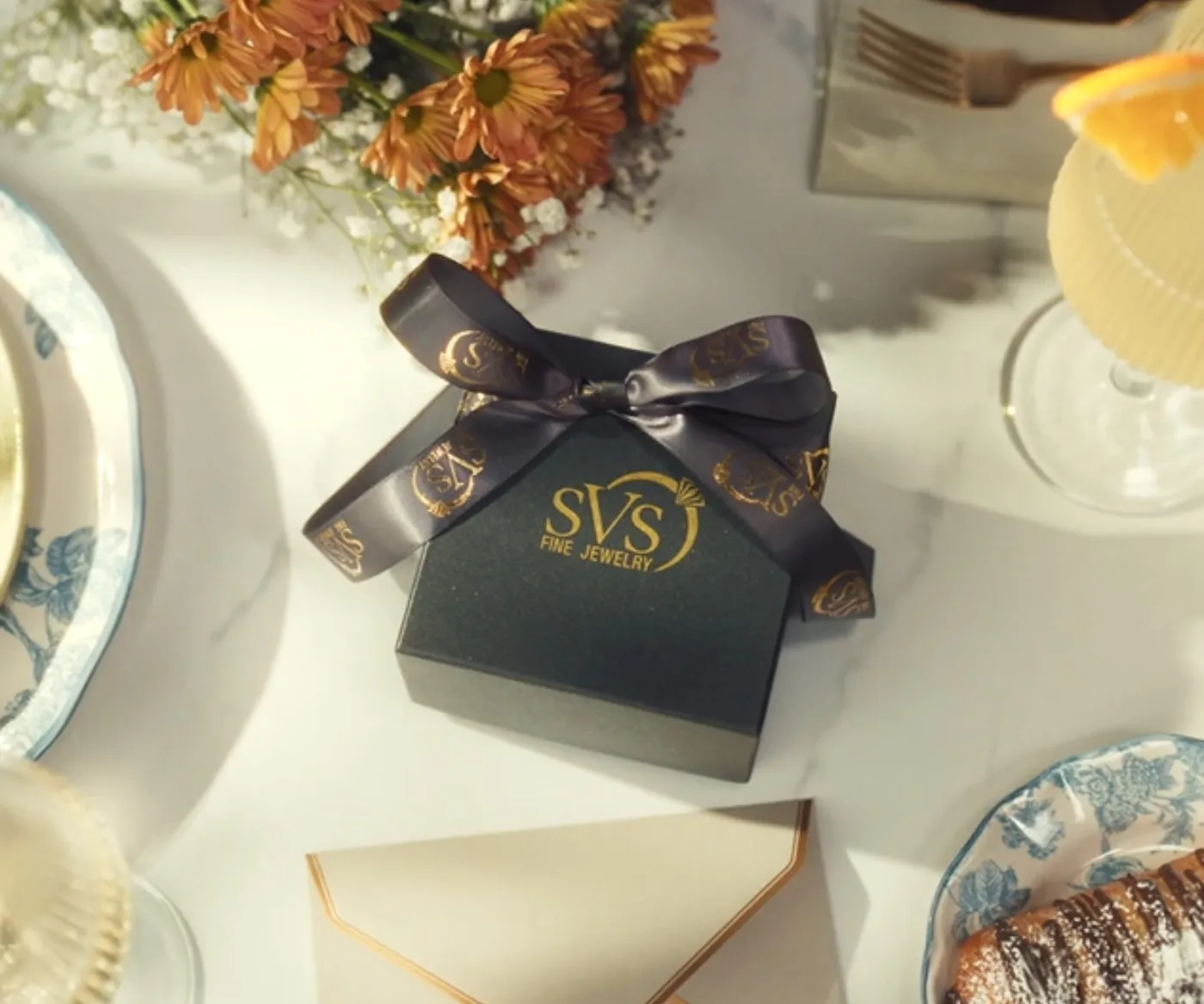 SVS Fine Jewelry gift box with signature gold logo and ribbon on a set table, Oceanside NY