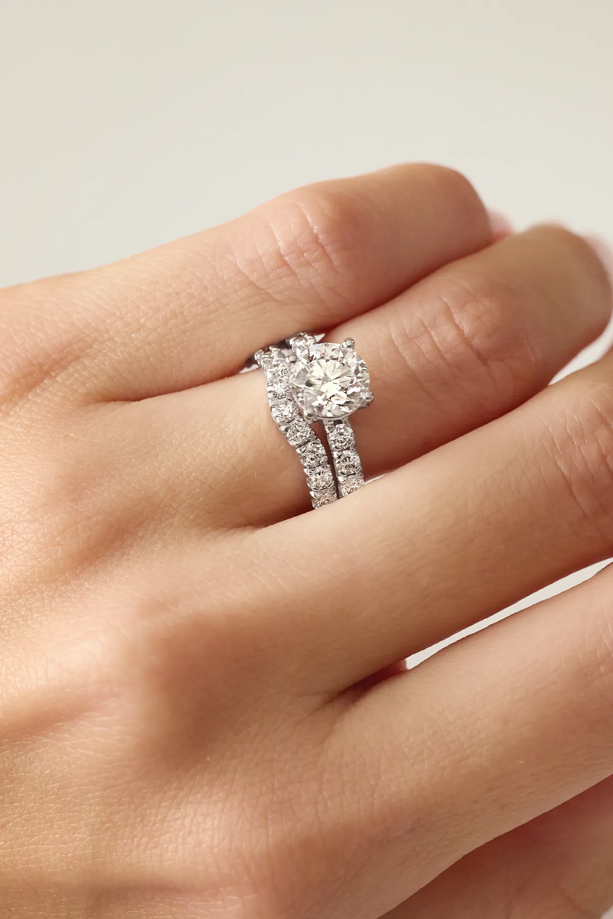 A hand wearing a diamond engagement ring with a matching diamond band.
