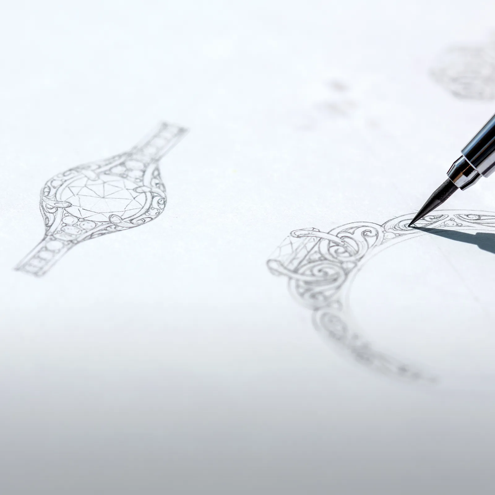 A detailed sketch of an ornate jewelry design with a pen drawing intricate patterns on paper.