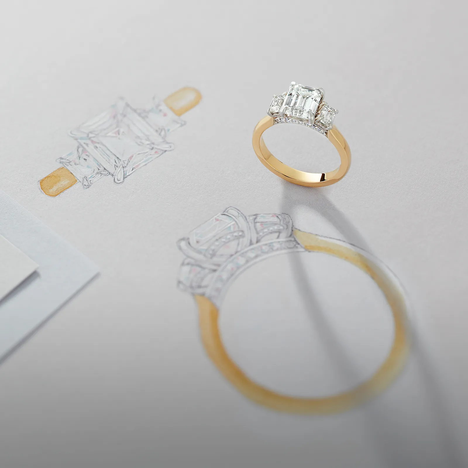 A gold ring with a large diamond is placed on a sketch of the same ring design.