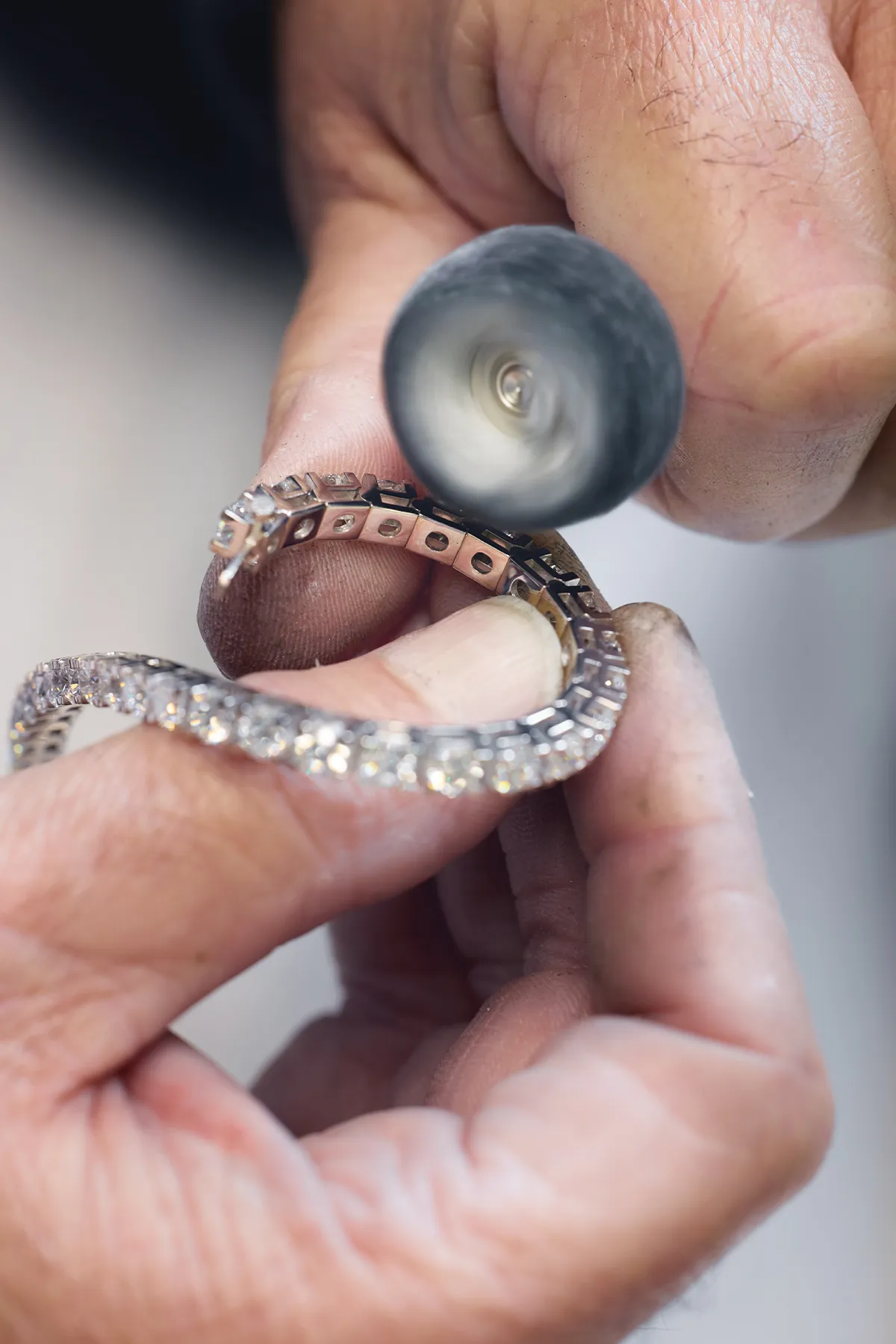 A person polishing a diamond bracelet with a rotary tool.