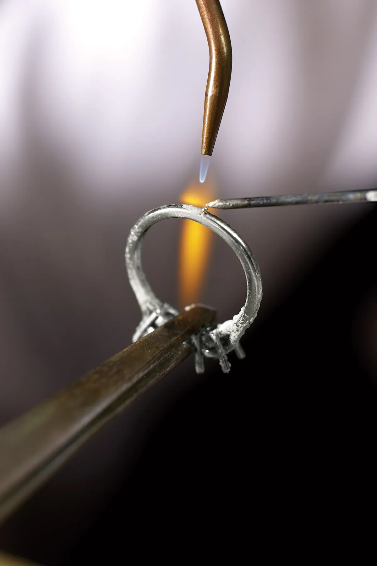 A jeweler soldering a ring with a flame and tools.