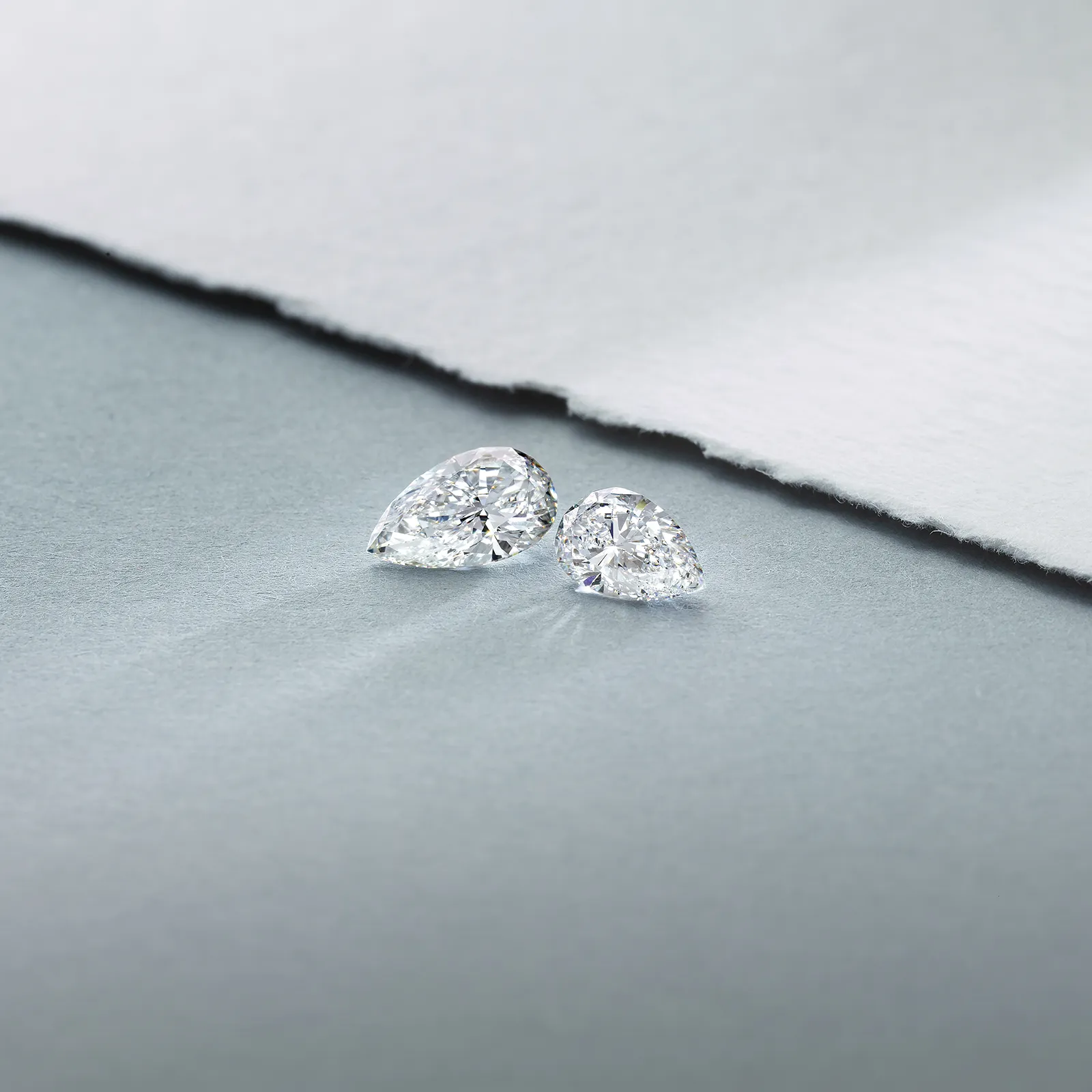 Two pear-shaped diamonds on a textured gray surface.