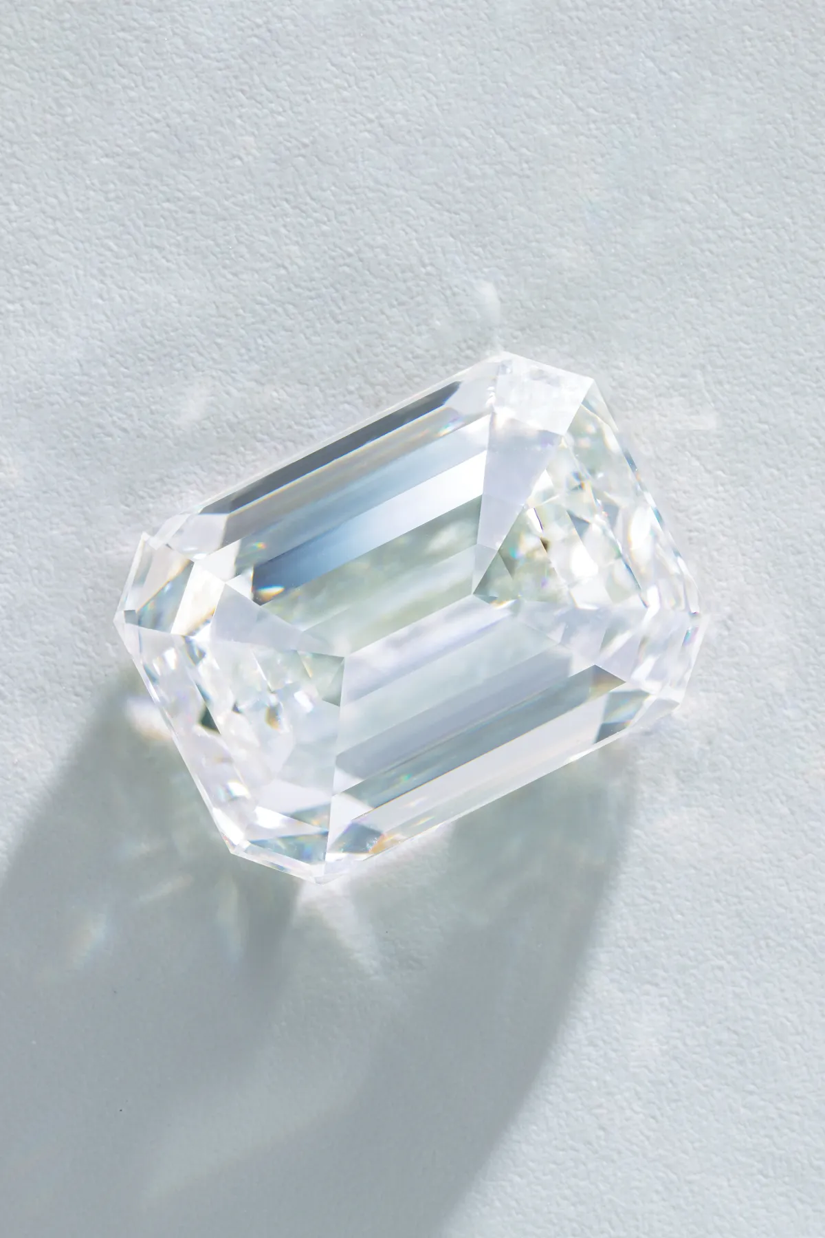 A clear, emerald-cut diamond casting a shadow on a textured surface.