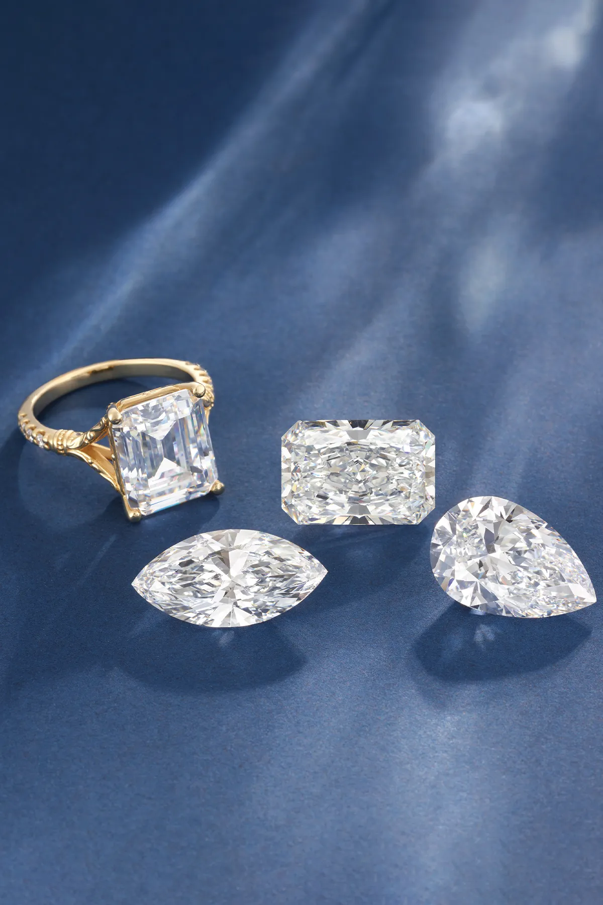 A gold ring with a large rectangular diamond and three loose diamonds on a blue surface.