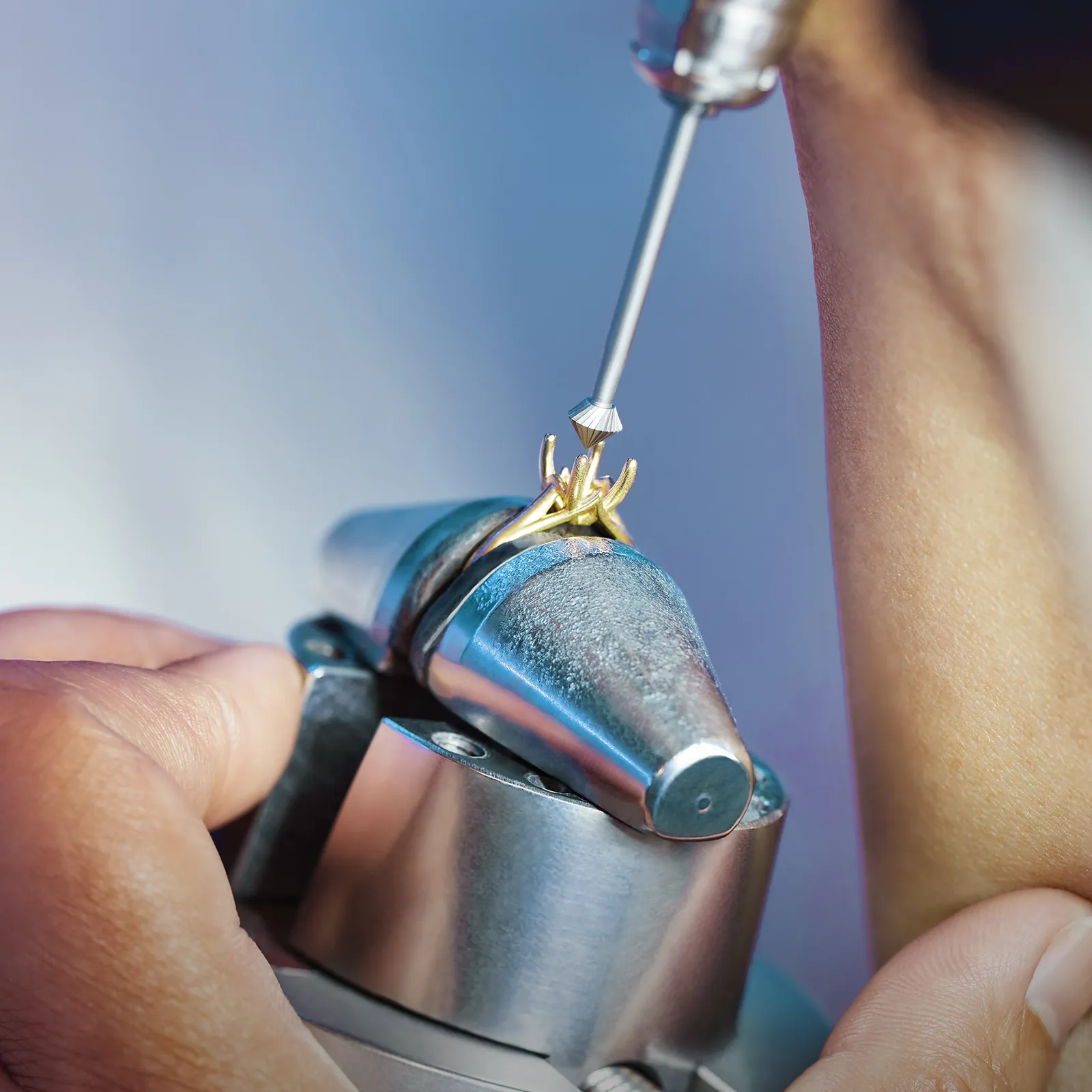A person using a tool to work on a gold ring setting held in a vise.