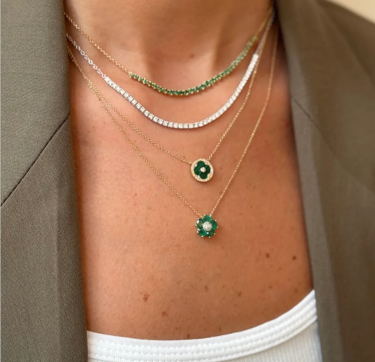 Layered gold necklaces with star and heart charms, worn with rings on a hand.