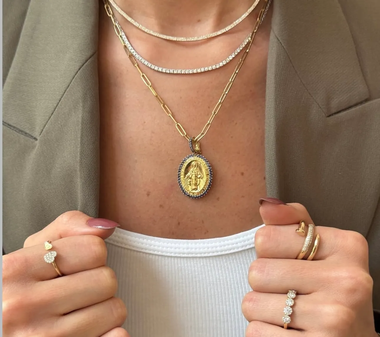 A young woman with curly hair rests her head on her hand, wearing a light blue top and delicate jewelry.