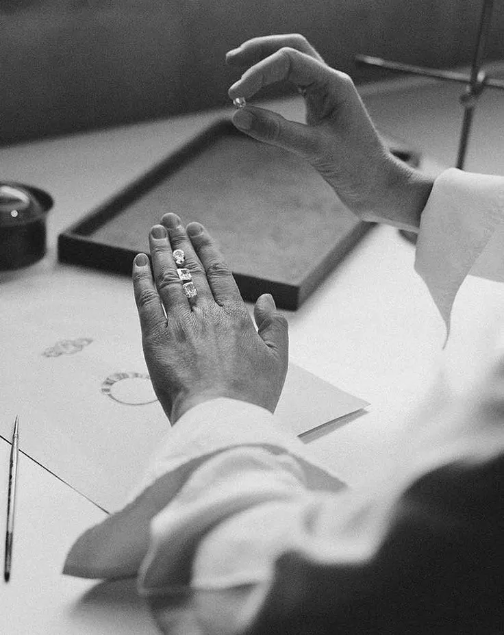 Close-up of a diamond engagement ring being held with tweezers against a dark fabric background.