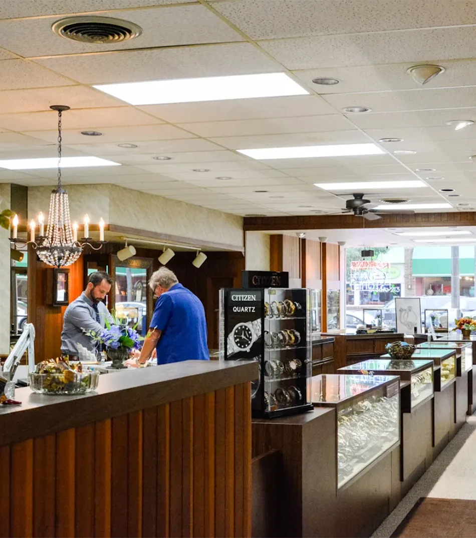 Inside Tennies Jewelry store, a customer consults with a staff member at the counter, surrounded by elegant displays.