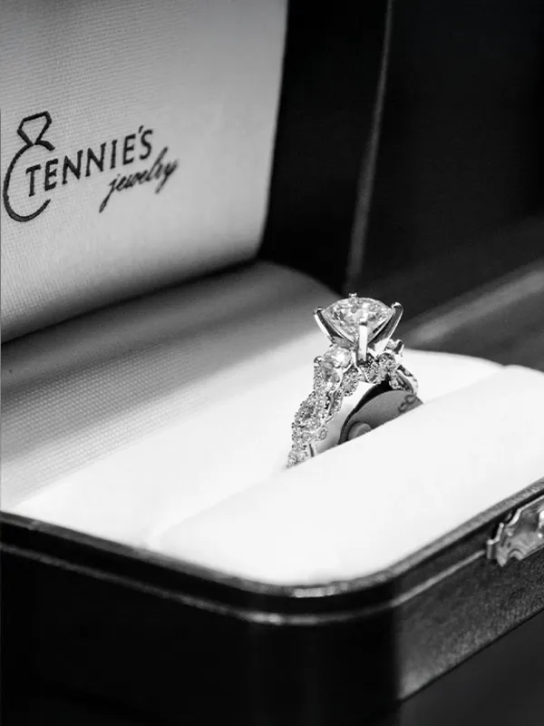 Two elegant gold rings with diamonds, featuring a large round and an emerald-cut center stone, displayed on soft fabric.