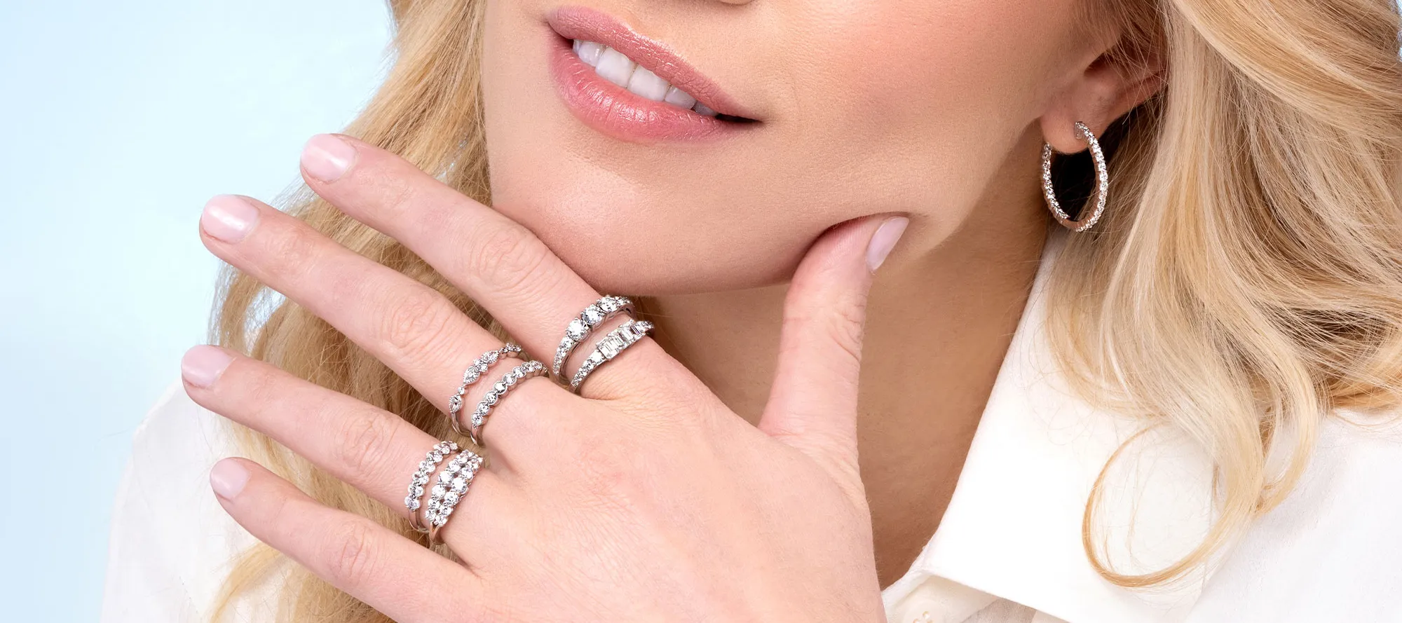 Close-up of a woman showcasing diamond rings and hoop earrings.