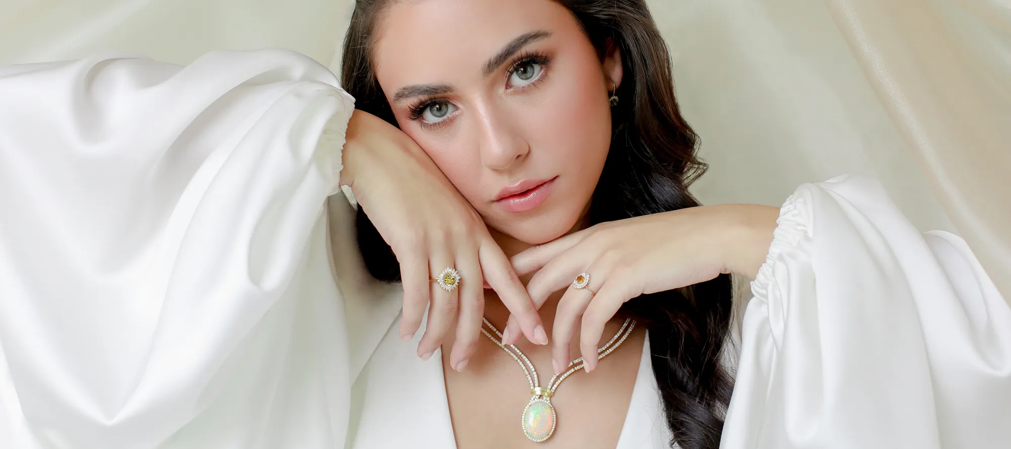 Model showcasing elegant jewelry, including a necklace and rings, against a soft white background.