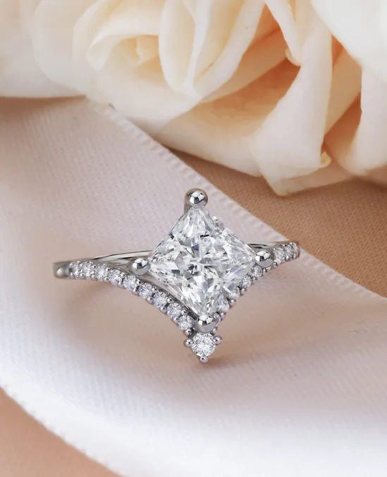 Elegant diamond engagement ring with a princess-cut center stone and smaller diamonds on the band, set against soft roses.