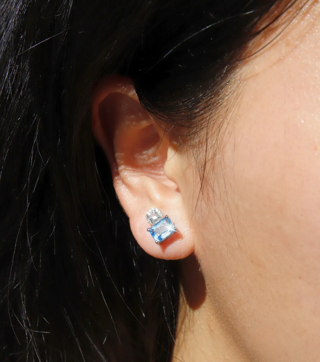 Close-up of a woman's ear wearing elegant blue and clear gemstone earrings.
