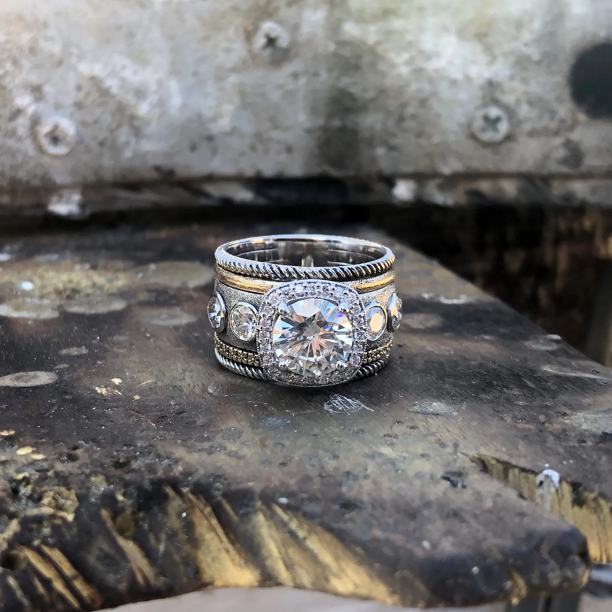 A diamond ring and a green ring sit on a black computer mouse, with a keyboard and colorful pens in the background.