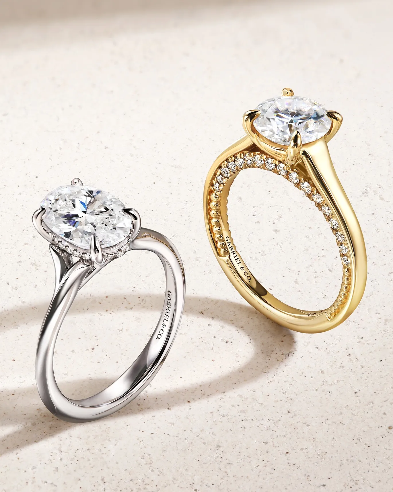 Two elegant engagement rings, one in silver and one in gold, featuring sparkling diamonds, displayed on a light surface.