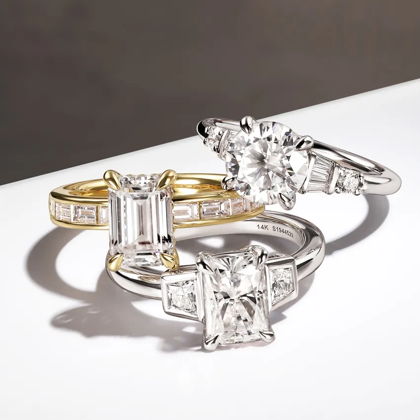 Three elegant diamond rings featuring round and emerald cut stones in yellow and white gold settings.