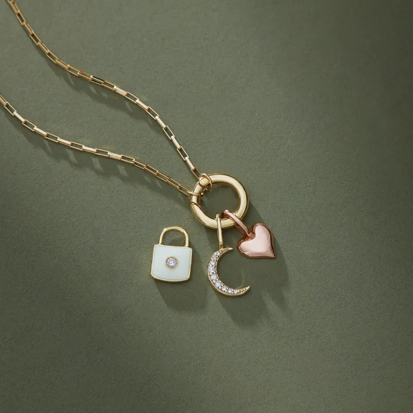 Gold necklace with charms: a padlock, crescent moon, and heart, displayed on a green background.