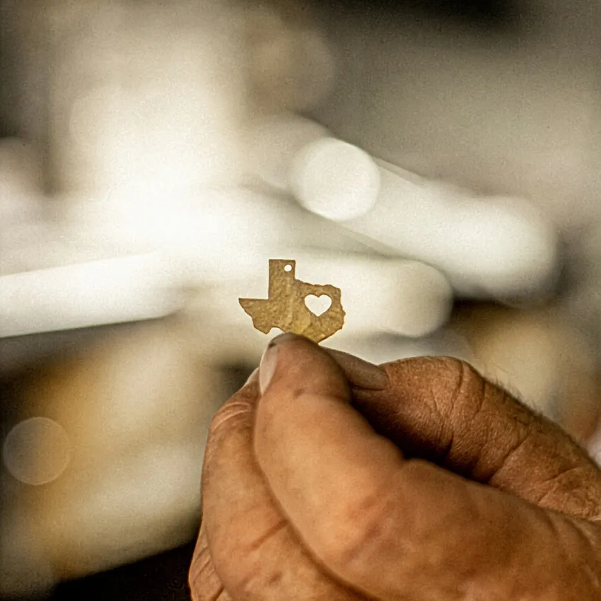 Hand holding a small Texas-shaped metal piece with a heart cutout, symbolizing Texas pride.