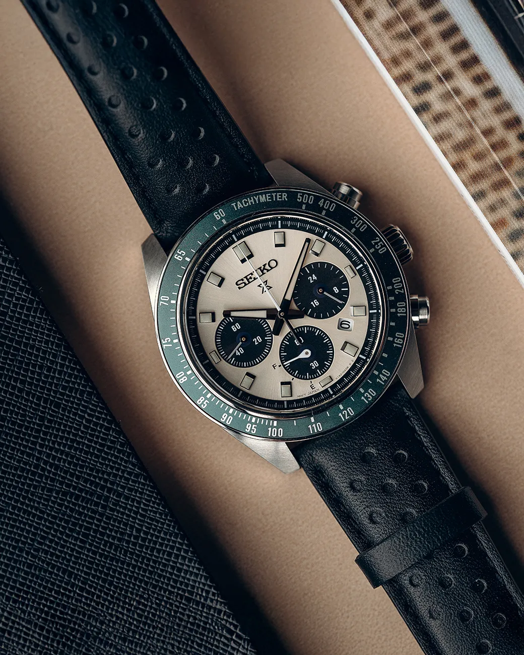 Seiko chronograph watch with black leather strap, displayed on a beige surface. 