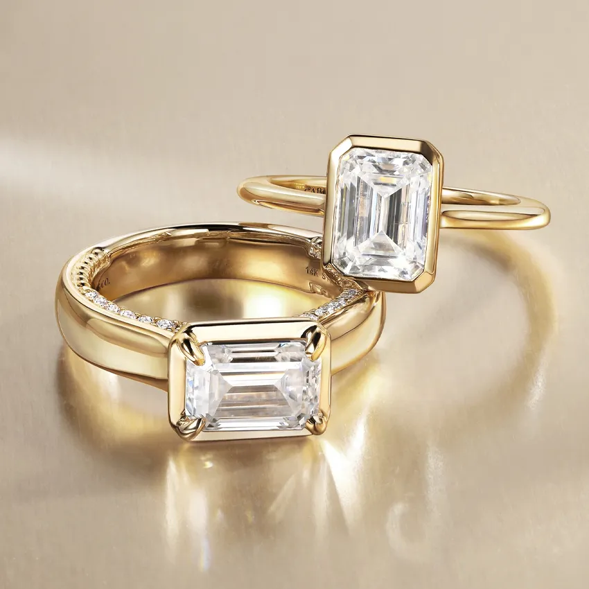 Two elegant gold engagement rings featuring emerald-cut diamonds, displayed on a soft background.