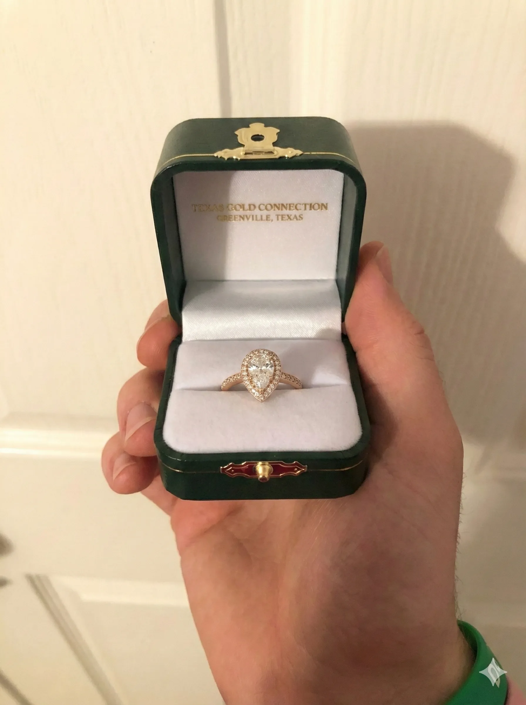 Engagement ring and green wax models on a sketchbook, with a pencil, showcasing jewelry design.