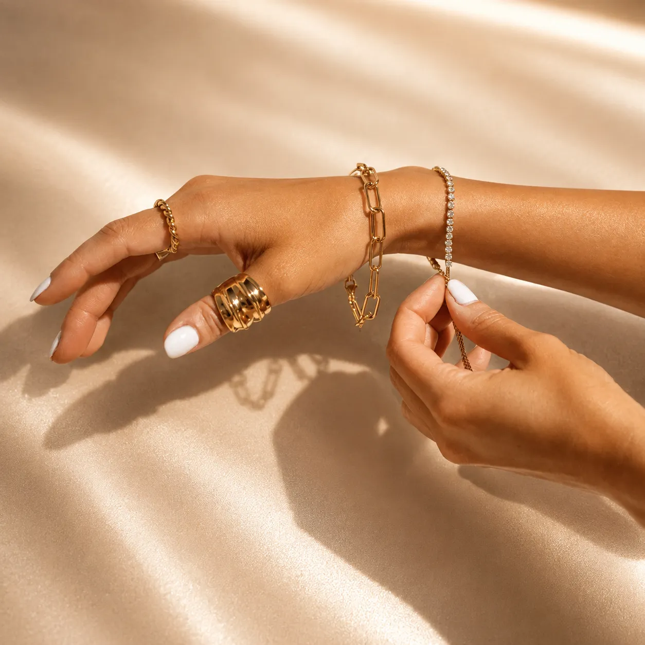 Gold bracelets and diamond tennis bracelet on elegant champagne background.