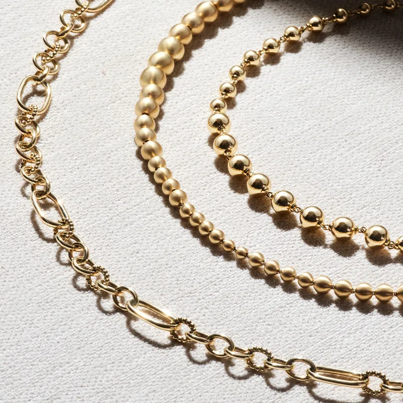 Three elegant gold chains of varying styles and sizes displayed on a textured surface. 