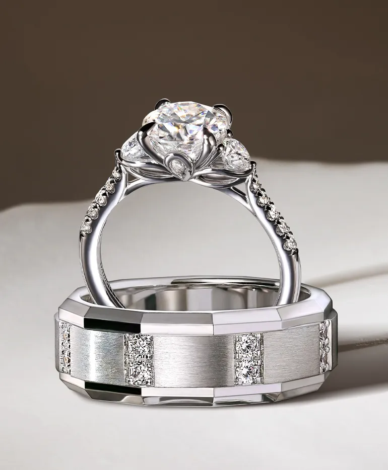Elegant diamond engagement ring with a floral design, paired with a sleek wedding band, displayed on a white surface.
