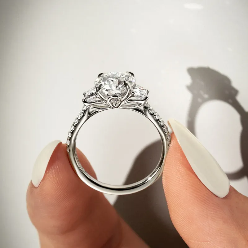 Elegant diamond engagement ring held between fingers, showcasing intricate design.