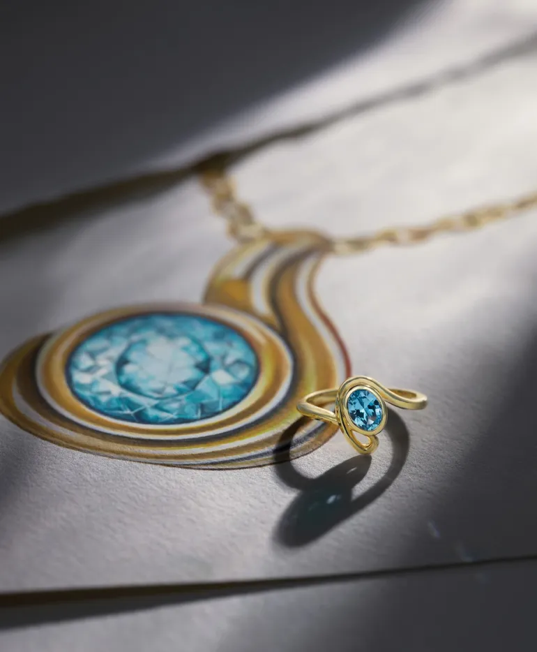 Gold ring with blue gemstone and a matching pendant, displayed on a drawing.