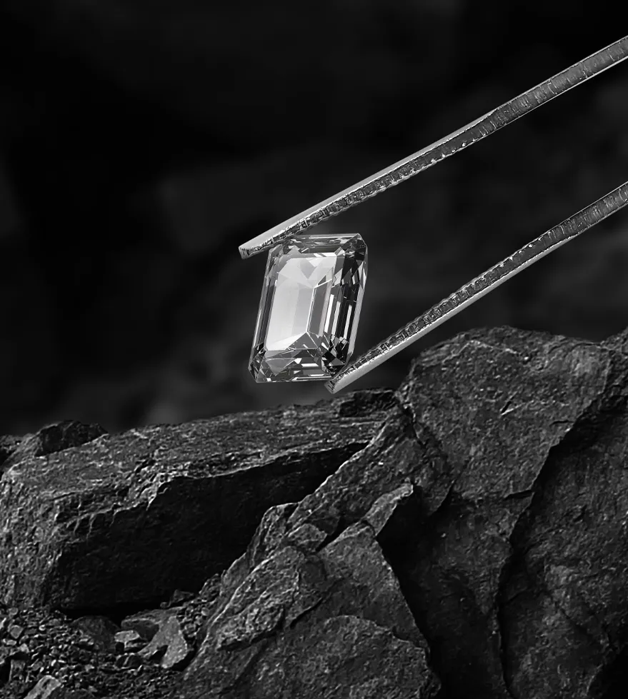 A diamond held with tweezers above dark rocks, showcasing its clarity and brilliance. Visit The Diamond Shop, Inc. for more.