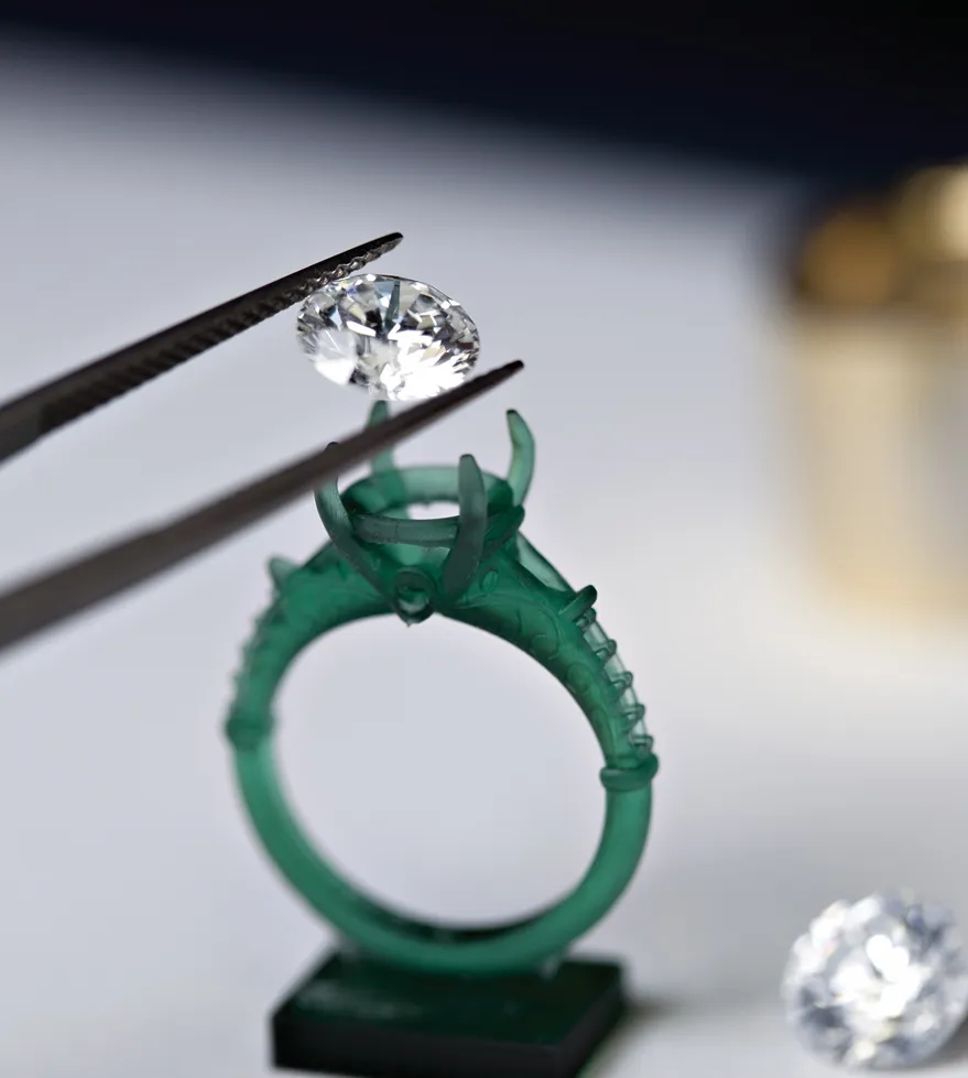 A diamond being placed into a green ring setting with tweezers, showcasing fine jewelry craftsmanship.