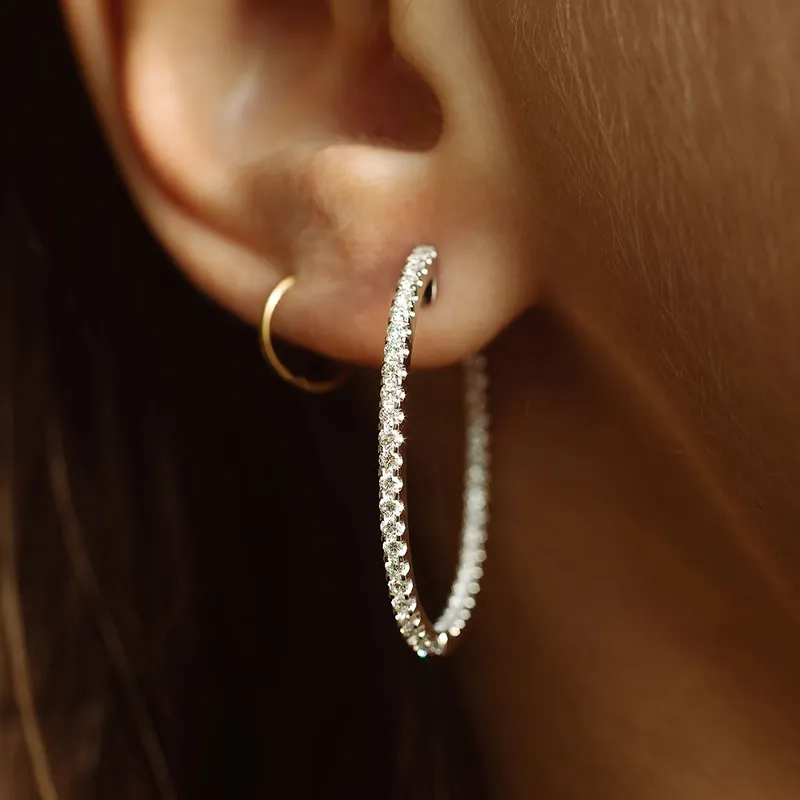 Close-up of a woman wearing sparkling diamond hoop earrings. Click to SHOP NOW for earrings at The Diamond Shop, Lewiston.
