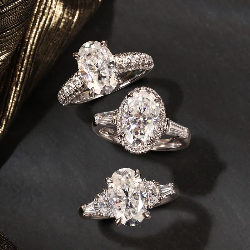 Three elegant engagement rings featuring oval diamonds and intricate settings, displayed on a dark surface. 