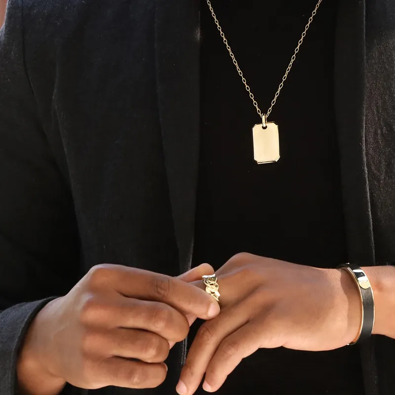 Stylish man wearing a gold dog tag necklace and rings, showcasing modern men's jewelry.