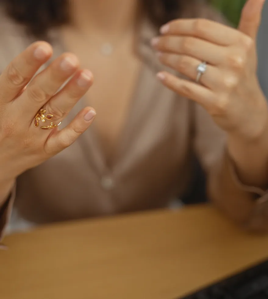 A woman showcasing a gold ring on her hand, with a diamond ring on her other hand, sitting at a desk.