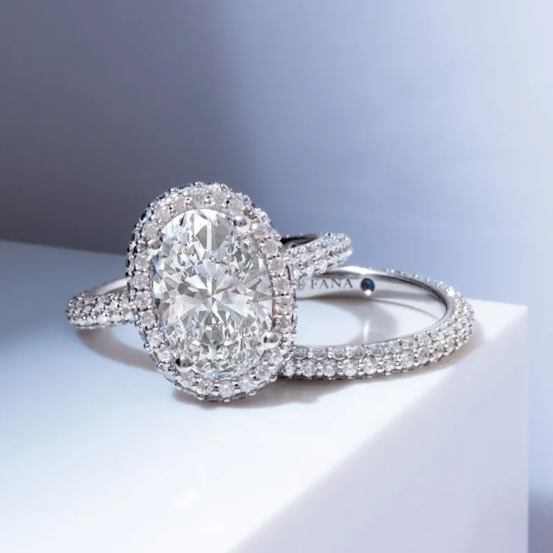 Elegant oval diamond engagement ring with a halo setting, displayed on a white surface.